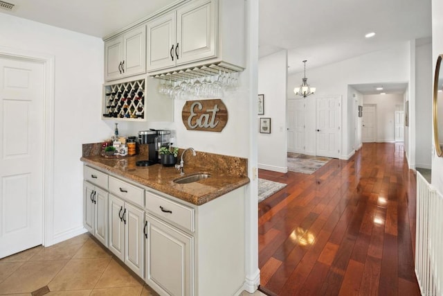 bar featuring sink, decorative light fixtures, vaulted ceiling, light wood-type flooring, and dark stone countertops