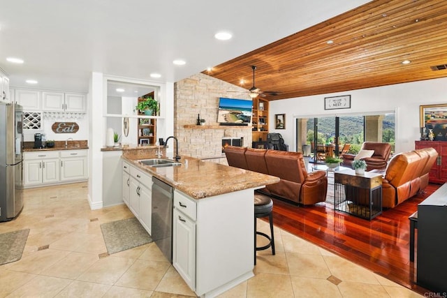 kitchen with appliances with stainless steel finishes, white cabinetry, sink, a kitchen breakfast bar, and light stone counters