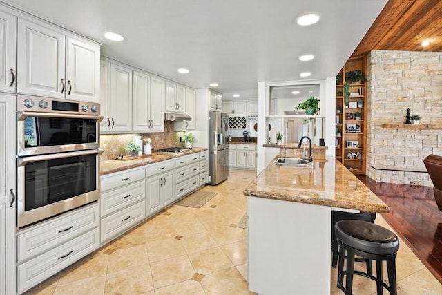 kitchen featuring sink, white cabinetry, light stone counters, stainless steel appliances, and a kitchen island with sink