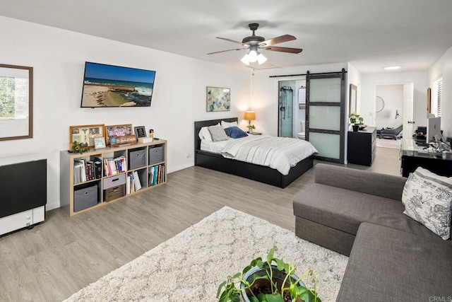 bedroom with ceiling fan, a barn door, and light wood-type flooring