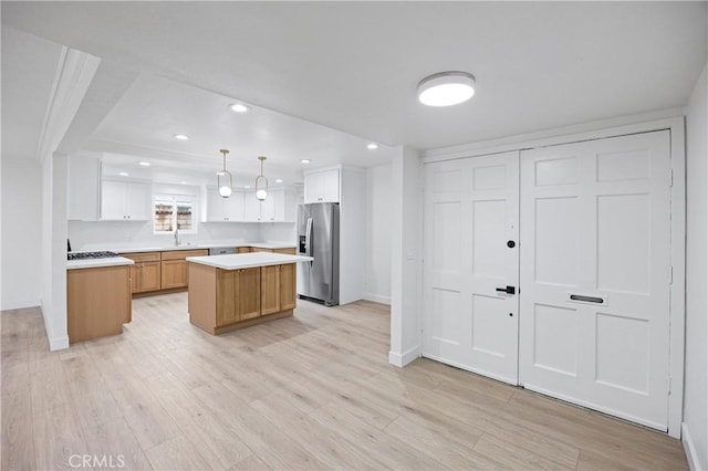 kitchen with white cabinetry, a center island, hanging light fixtures, stainless steel fridge, and light hardwood / wood-style floors