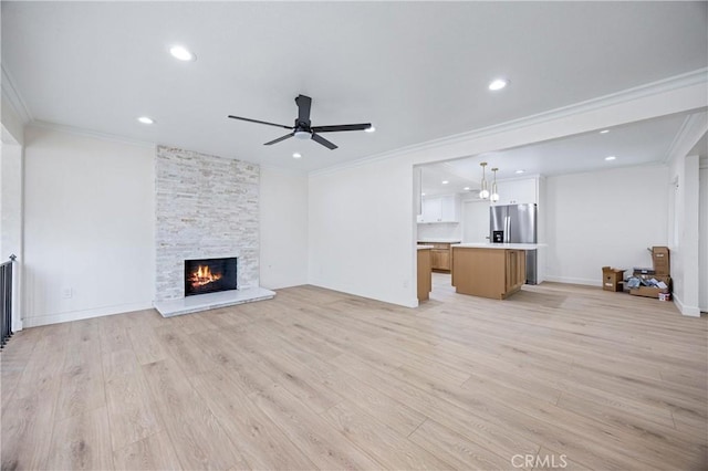 unfurnished living room with crown molding, a stone fireplace, ceiling fan, and light wood-type flooring