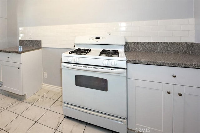 kitchen with dark stone countertops, white range with gas stovetop, white cabinets, and backsplash