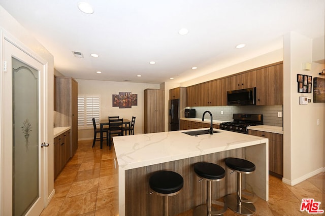 kitchen with an island with sink, sink, decorative backsplash, and black appliances