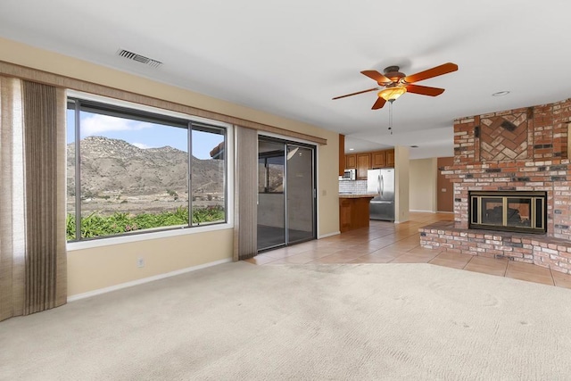 unfurnished living room with a mountain view, light colored carpet, ceiling fan, and a brick fireplace