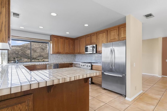 kitchen with light tile patterned flooring, tasteful backsplash, tile countertops, kitchen peninsula, and stainless steel appliances