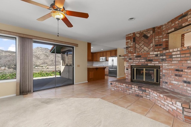 unfurnished living room with a mountain view, light tile patterned floors, ceiling fan, and a brick fireplace