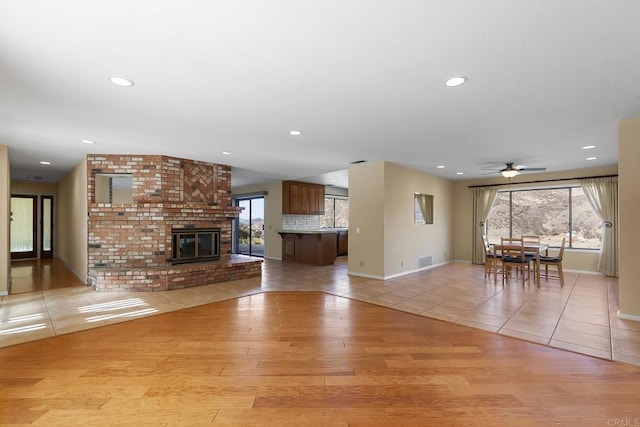 unfurnished living room with ceiling fan, a fireplace, and light hardwood / wood-style flooring