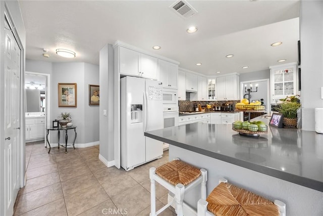 kitchen with white appliances, a kitchen bar, white cabinetry, kitchen peninsula, and decorative backsplash