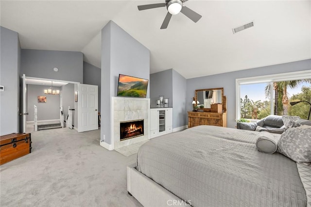 carpeted bedroom with a tile fireplace, vaulted ceiling, and ceiling fan with notable chandelier