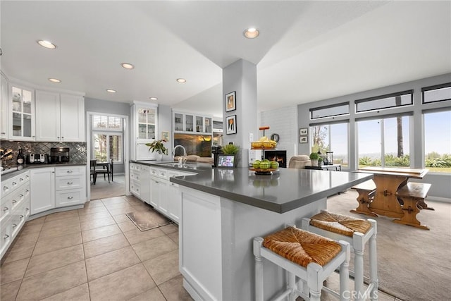 kitchen with a kitchen breakfast bar, decorative backsplash, light tile patterned floors, sink, and white cabinetry