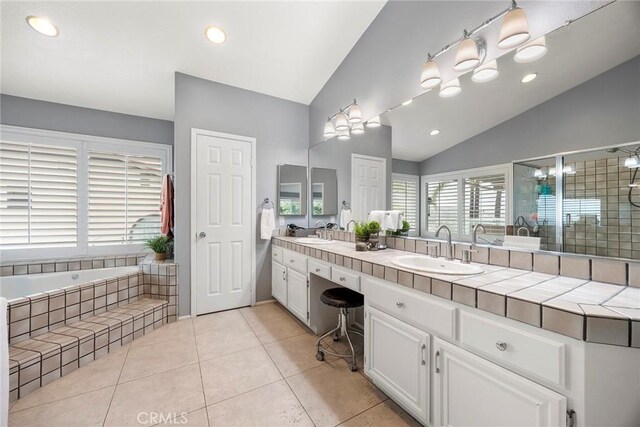 bathroom featuring tile patterned floors, vanity, lofted ceiling, and tiled tub