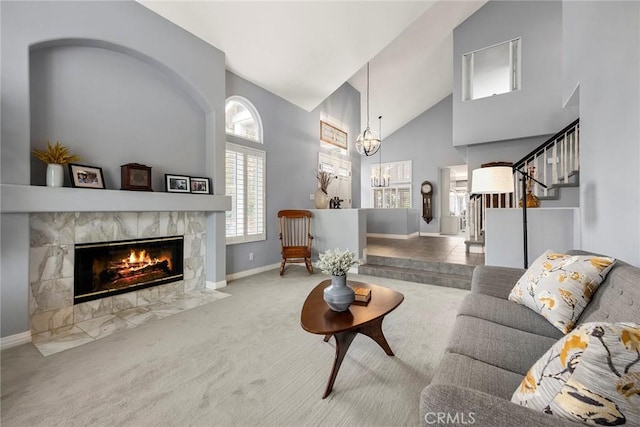 living room featuring a fireplace, high vaulted ceiling, light carpet, and a notable chandelier