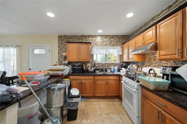 kitchen with dark stone countertops, sink, decorative backsplash, and white gas stove