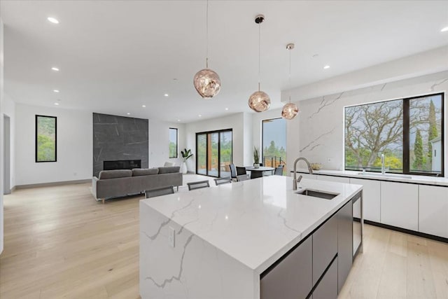 kitchen with hanging light fixtures, an island with sink, light stone countertops, and sink