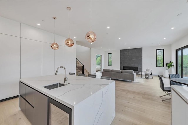 kitchen featuring sink, hanging light fixtures, an island with sink, light stone countertops, and white cabinets