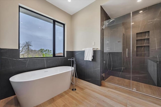 bathroom featuring wood-type flooring, plus walk in shower, and tile walls