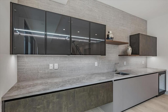 kitchen featuring light stone countertops, sink, decorative backsplash, and light wood-type flooring