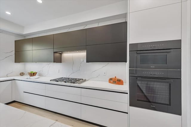 kitchen featuring stainless steel gas cooktop, tasteful backsplash, white cabinetry, light wood-type flooring, and double oven