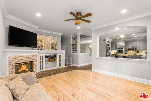 living room with hardwood / wood-style flooring, crown molding, ceiling fan with notable chandelier, and a fireplace