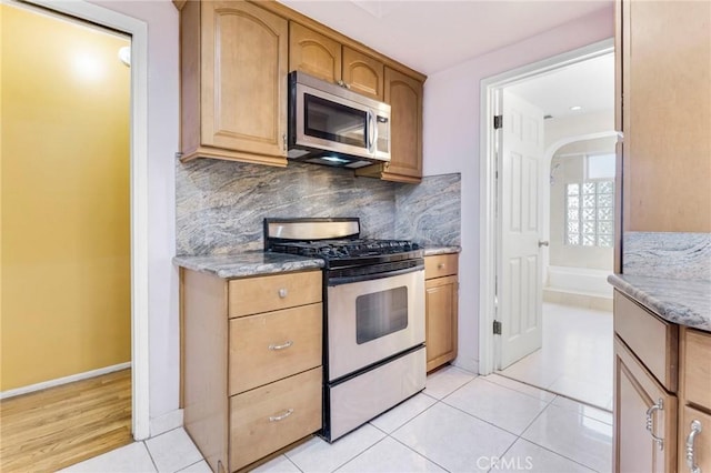 kitchen with appliances with stainless steel finishes, stone countertops, decorative backsplash, and light tile patterned floors