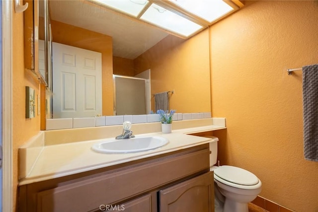 bathroom with a shower with door, vanity, a skylight, and toilet