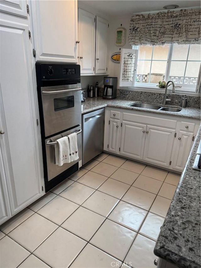 kitchen featuring appliances with stainless steel finishes, sink, light tile patterned floors, and white cabinets