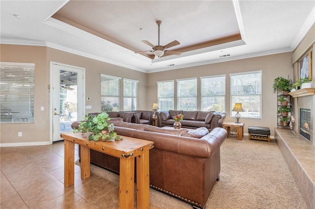 living room featuring a tray ceiling, crown molding, a fireplace, light tile patterned flooring, and ceiling fan