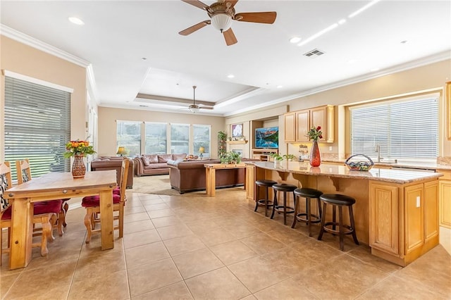 kitchen with a center island, a tray ceiling, ornamental molding, light stone countertops, and light brown cabinetry