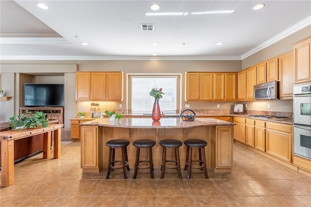 kitchen featuring appliances with stainless steel finishes, a kitchen breakfast bar, a center island, light stone countertops, and light brown cabinetry