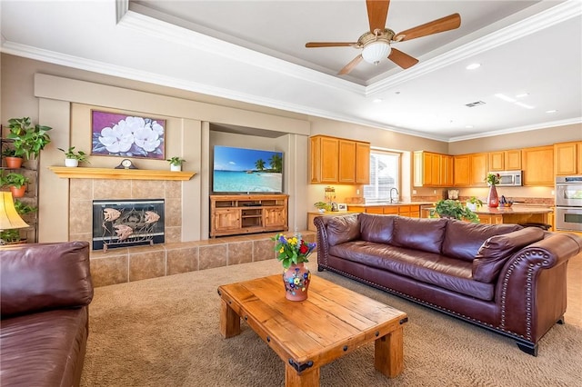 living room with ornamental molding, a tray ceiling, light carpet, and a tiled fireplace