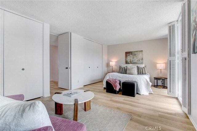 bedroom with multiple closets, a textured ceiling, and light hardwood / wood-style floors