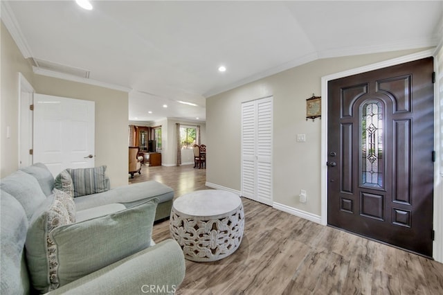 entrance foyer featuring lofted ceiling, ornamental molding, and light hardwood / wood-style flooring