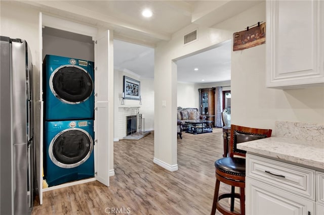 laundry area featuring stacked washer / drying machine, light hardwood / wood-style floors, and a brick fireplace