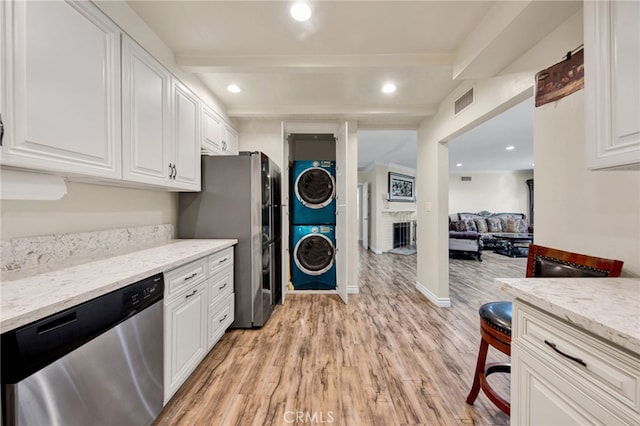 kitchen with appliances with stainless steel finishes, white cabinetry, stacked washer / drying machine, light stone counters, and light wood-type flooring