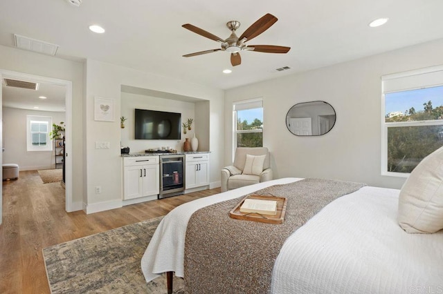 bedroom featuring wine cooler, ceiling fan, bar area, and light wood-type flooring