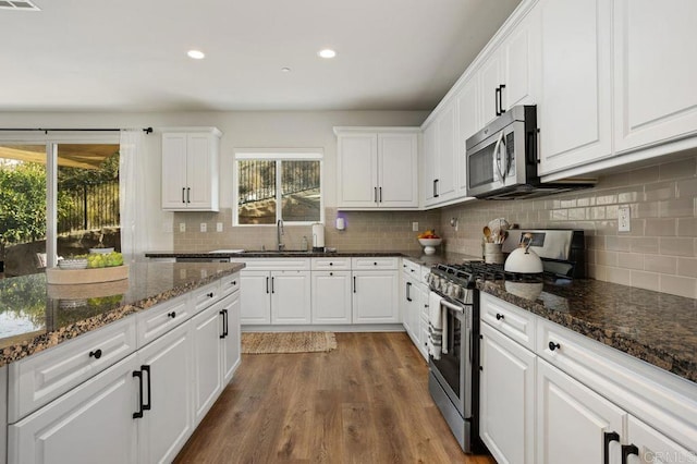 kitchen with white cabinetry, appliances with stainless steel finishes, sink, and dark stone countertops