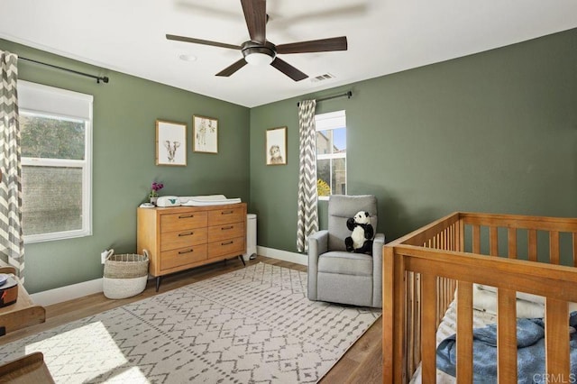 bedroom with wood-type flooring, a nursery area, and ceiling fan