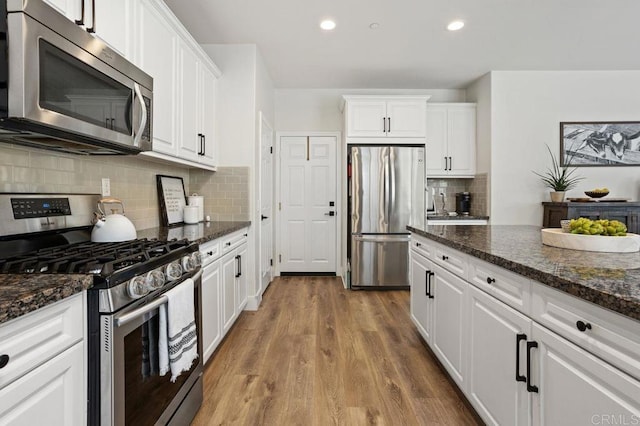 kitchen with stainless steel appliances, dark stone counters, and white cabinets