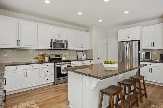 kitchen with dark stone countertops, appliances with stainless steel finishes, a kitchen island, light hardwood / wood-style floors, and white cabinets