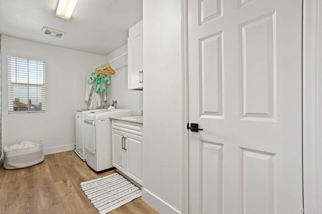 laundry area with cabinets, separate washer and dryer, and light hardwood / wood-style flooring