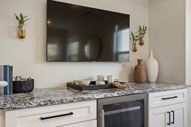 bar with wine cooler, white cabinets, and stone countertops