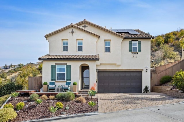 mediterranean / spanish-style home with fence, stucco siding, decorative driveway, and roof mounted solar panels