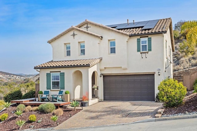 mediterranean / spanish home with a tiled roof, solar panels, stucco siding, and decorative driveway