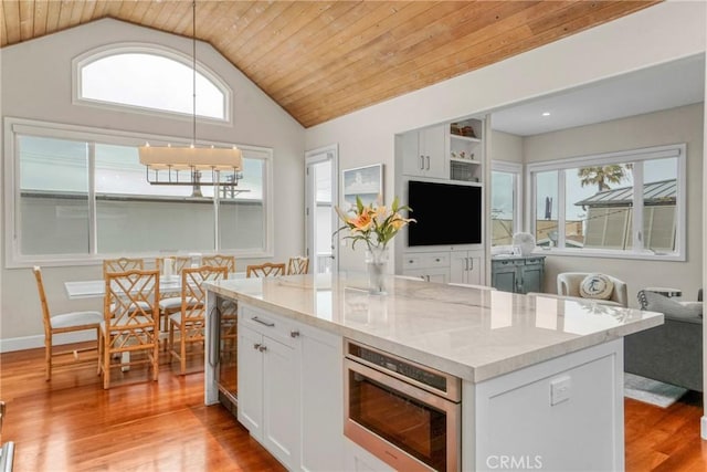 kitchen featuring white cabinetry, light hardwood / wood-style flooring, stainless steel microwave, pendant lighting, and light stone countertops