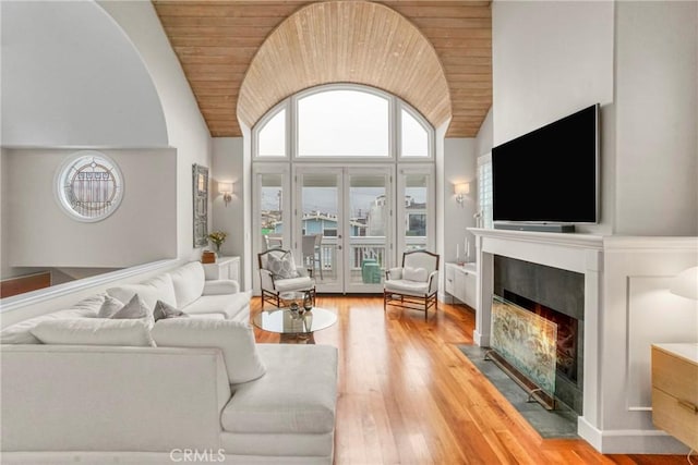 living area with wood finished floors, high vaulted ceiling, a fireplace with flush hearth, french doors, and wooden ceiling