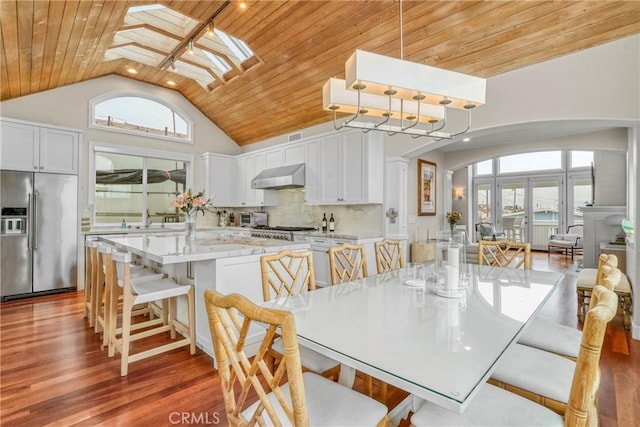 dining space with high vaulted ceiling, dark wood-type flooring, wood ceiling, and a skylight