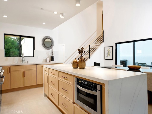 kitchen with sink, stove, a center island, light brown cabinetry, and oven