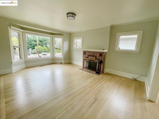 unfurnished living room featuring ornamental molding, a tiled fireplace, and light hardwood / wood-style flooring