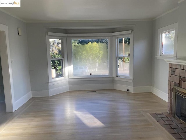 unfurnished dining area featuring a tiled fireplace, ornamental molding, light hardwood / wood-style floors, and a healthy amount of sunlight